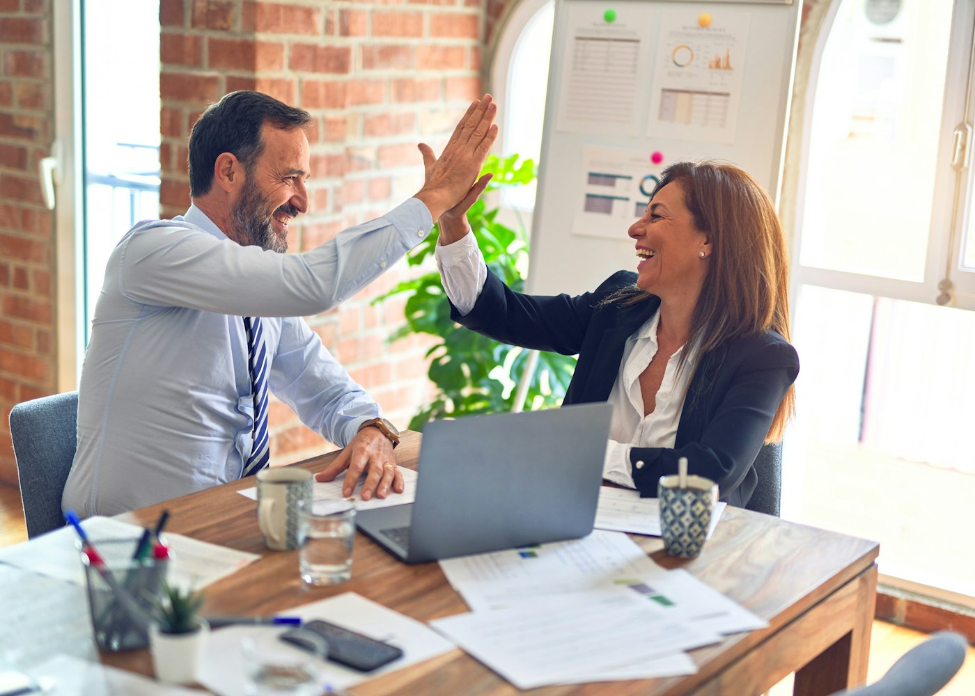 Two business owners high-fiving to celebrate a new client win at their desk